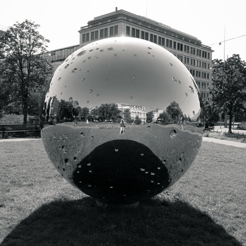 Black and white picture of a big metallic ball. The photographer can be seen in its reflection.