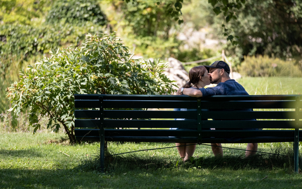 Picture of a couple sitting on a bench, kissing each other.