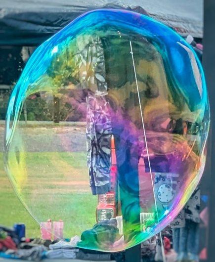 A large bubble floats in front of a gazebo with items for sale