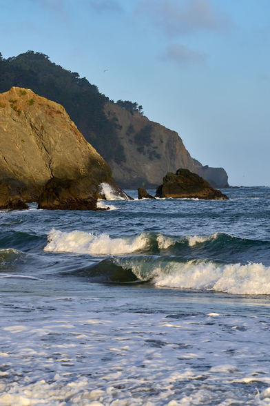 Long shot of layers of headlands with waves crashing on the inferred beach in the foreground.