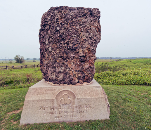 Large boulder made of smaller rocks stuck together on a white pedestal which says 20th mass infantry