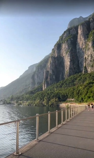 A footpath along the beautiful lake (left side) with sunshine and a gorgeous mountain on the right side of the landscape.