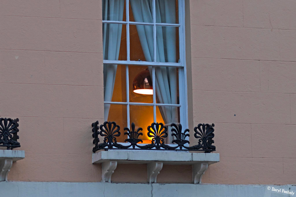 A lamp through a tall period window, at dusk. 