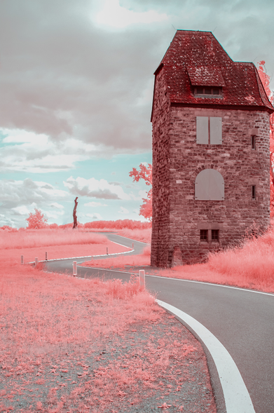 Das Bild zeigt eine Infrarotfotografie  von einem kurvigen Asphaltweg, der an einem alten, roten Stein-Turm vorbeiführt, unter einem leicht bewölkten Himmel, der in einer unnatürlichen rosa Farbe gehalten ist.

Das Bild zeigt einen kurvigen Asphaltweg, der sich durch eine Landschaft schlängelt, die in einem unnatürlichen, rosa Farbton gehalten ist.  Der Weg ist mit weißen Markierungen versehen. Rechts am Bildrand steht ein hoher, quadratischer Turm aus rotem Stein. Das Dach des Turms ist mit roten Ziegeln gedeckt. An den Seiten des Turms befinden sich kleine Fensteröffnungen, teilweise mit Holzschiebern verschlossen.  Es gibt eine größere Öffnung in der unteren Hälfte des Turms, ebenfalls mit einem Holzschieber.  Links im Bild, in der Ferne, befindet sich ein einzelner, kahler Baumstamm. Er steht auf einem leicht erhöhten Feld mit rosa Vegetation. Der Himmel ist bedeckt mit weichen, hellgrauen Wolken. Die gesamte Szenerie wirkt ruhig und etwas gespenstisch durch die ungewöhnliche Farbgebung.  Die Stimmung ist geheimnisvoll und melancholisch. Das Rosa gibt dem Bild einen surrealen Touch.
