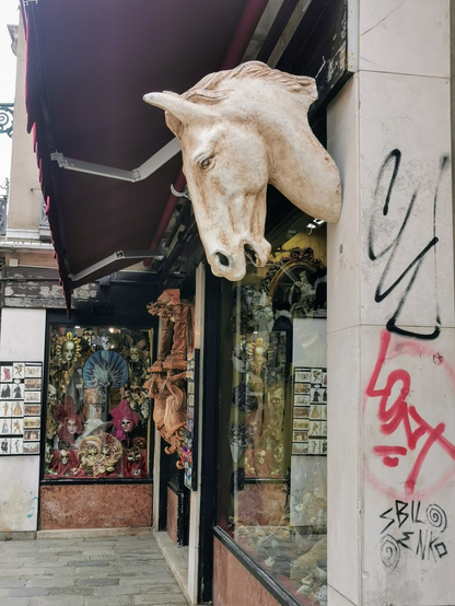 Ein Geschenkeladen in Venedig. An einer Mauer neben dem Schaufenster hängt die Skulptur eines Pferdekopfes.
