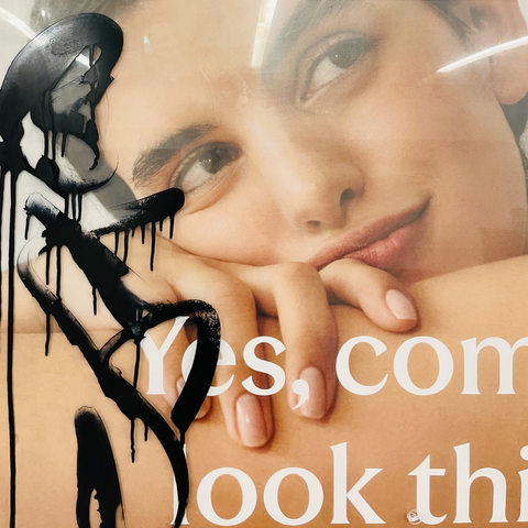 Bold black paint drips over an advertising image poster featuring a smiling face and a hand with manicured nails. Large, white text can be seen on the bottom of the image.