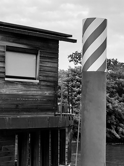 Fenêtre blanche fermée sur une structure en planches. Contraste souligné par le noir et blanc. Fleuve et arbres en.fond immédiat.