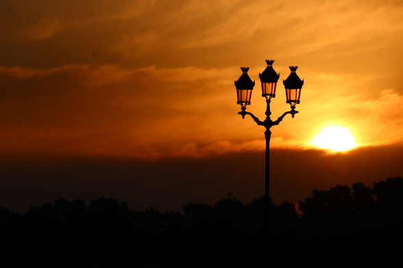 Photo prise au lever du jour, sur les quais bordelais.
Concrètement, c'est un format paysage, deux tiers sont pris par le ciel, très orange et jaune.
Le tiers bas est très sombre.
Un lampadaire en fer forgé, à 3 têtes, est bien visible.
Juste à côté, le soleil levant.