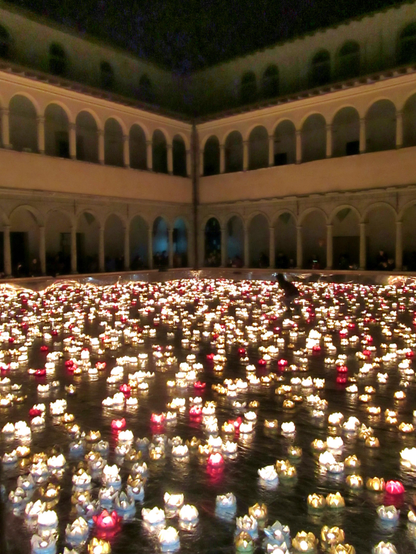 The image depicts a nighttime scene in a courtyard surrounded by a building with arched windows and columns. The courtyard is filled with numerous floating candles in various colors, predominantly white, red, and gold, creating a serene and illuminated atmosphere. The candles are arranged in a seemingly random pattern across the water's surface, reflecting the light and adding to the ambiance. In the background, the building's architecture is visible, with multiple arches and a second level that mirrors the first. A person is seen walking through the area, adding a sense of scale and human presence to the scene. The overall effect is a tranquil and visually striking display of light and architecture.

Provided by @altbot, generated privately and locally using Ovis2-8B

🌱 Energy used: 0.175 Wh