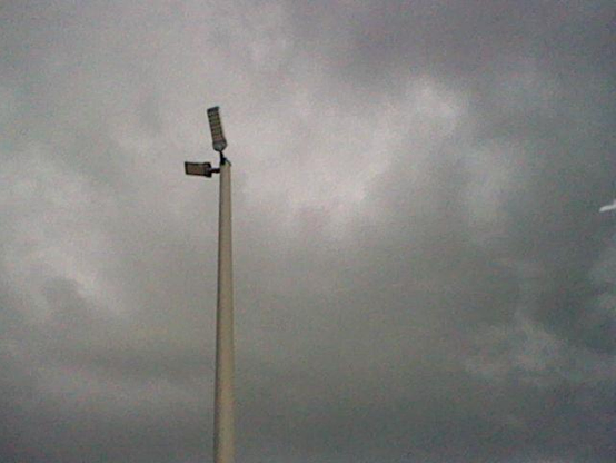 Looking up at a tall metal light pole with two large lamps on an overcast day. Very grey.