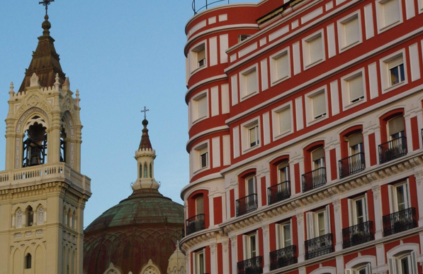 Building in red and white stone patterns with identical windows next to a church on Calle de Alcalá in Madrid - Spain.