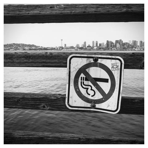 No smoking sign on a pier's railing. The Seattle waterfront and the space needle in the background.