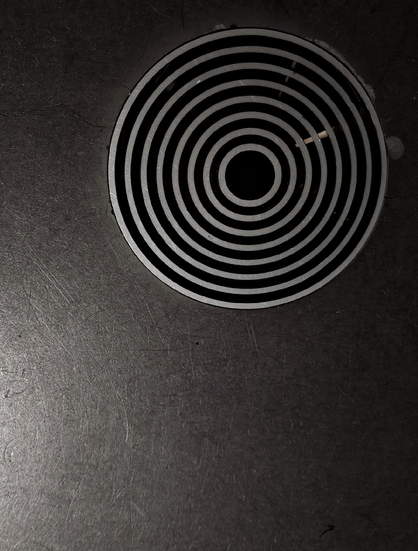 Close up of a slightly scratched dark vinyl floor with a round drain covered by a grill of bright concentric metal rings.