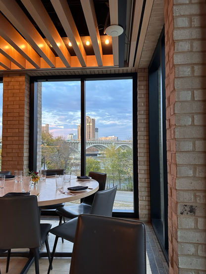 A round table is set with napkins, glasses and silverware. Through the window behind is a view of the Mississippi River and part of a bridge crossing it.