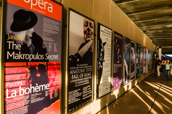 This is a wall at the front of the Sydney Opera House with advertising on it for coming events. These vertical panels recede into the distance, where a man is looking at one of them, and a woman is walking along.