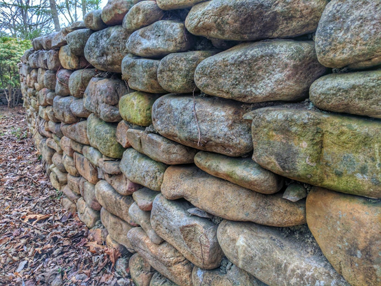 A stone wall with long slender rounded rocks in different sizes