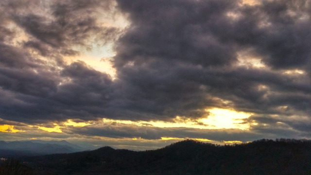 A sunset view with mountains in the background a glowing sun and dark clouds in the foreground