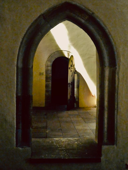 Blick durch einen frühgotischen Bogen in der Klosterkirche Bursfelde auf eine geöffnete Tür. Von oben fällt ein Lichtstrahl herab in den sakralen Raum.