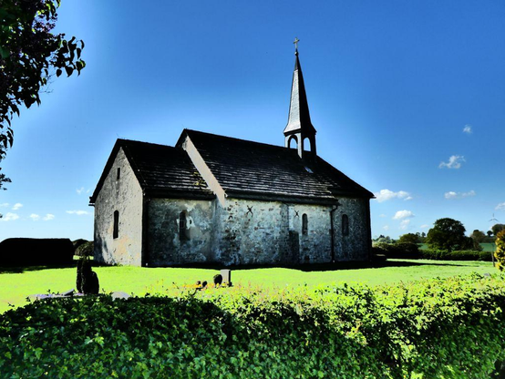 Die spätromanische Dorfkirche von Hattensen in der Ottensteiner Hochebene. Sie wird umgeben vom Friedhof der Gemeinde Ottenstein. Im Mittelalter muss hier einmal ein Dorf gewesen sein, das wüst gefallen ist und von dem nur die Kirche übriggeblieben ist, die heute als Friedhofskapelle genutzt wird. Anmutig liegt das Kirchlein dar, umgeben vom Friedhof. Auf diesem Friedhof befindet sich auch das Grab von Antonio Congo, einem wandernden Tischlergesellen aus Afrika, der im 19. Jahrhundert als Sklave nach Brasilien verschleppt und
dort an Kindes statt von einem Hamburger Kaufmann angenommen wurde und nach Hamburg gelangte. Er erlernte das Tischlerhandwerk, ging auf die Walz und verstarb auf der Ottensteiner Hochebene. Er fand auf diesem Friedhof seine letzte irdische Ruhestätte.