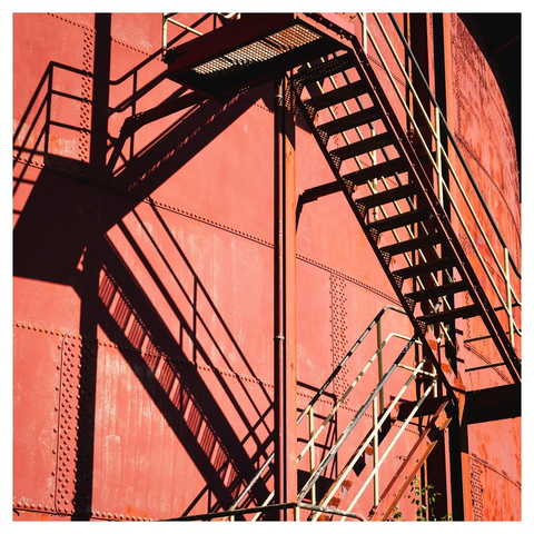 Stählerne Treppen und deren dunkle Schatten führen im zickzack eine stählerne, rostrot gestrichene Industrieanlage hinauf