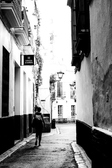 Black and white photo of a narrow street, with a person walking 