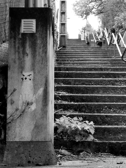 En ville, vue vers un escalier ascendant, un chat peint à côté des premières marches semble monter la garde