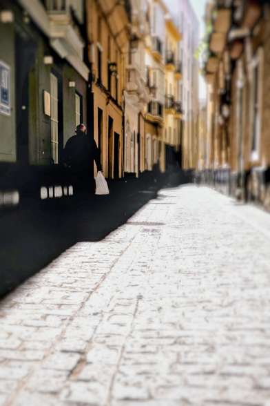 A narrow street with colorful houses left and right and a person walking in the shade.