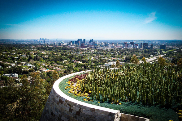 The image presents a panoramic view of a cityscape under a clear blue sky. In the foreground, there is a well-maintained garden with a variety of plants, including tall cacti and other succulents, arranged in a curved pattern along a stone wall. The garden is lush and green, with some yellow flowers adding a pop of color. Beyond the garden, the city unfolds with a mix of residential and commercial buildings, including several tall skyscrapers that form the city's skyline. The buildings are spread out across the landscape, with roads and green spaces interspersed among them. The overall scene is bright and sunny, with the city stretching out towards the horizon.
Provided by @altbot, generated privately and locally using Ovis2-8B