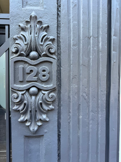 The house number for a building. The number 128 is engraved with some fancy curlicues around it. It’s probably made of stone but has since been painted it gentrification grey.