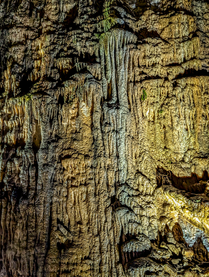 The intricate and textured surface of a natural cave formation, illuminated to highlight its features. The dominant colors are earthy tones of brown, gold, and beige, with hints of grayer and darker shades, especially in the crevices.

The surface is highly irregular and is covered in countless stalactites and flowstone formations. There are numerous vertical, corrugated patterns, due to the flow of water over a long period of time.

Erdmannshöhle cave, Germany.
