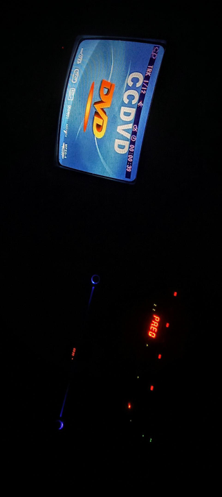 The photograph composed in a dark Studio, showcases a brightly lit DVD player screen at the top. The screen displays "CCDVD" in large, bold, orange letters on a blue background, with additional text including "TRK 1/12" and a time indicator "00:03:39." The DVD player also shows compatibility with "MPEG-4" and "H.264" formats. Below the screen, a dimly lit dashboard is visible, featuring a red digital display showing "PR.EQ" and a blue illuminated knob. The overall scene is set in an extremely low-light environment, emphasizing the DVD player's screen and dashboard controls.

 Ovis2-8B

🌱 Energy used: 0.176 Wh