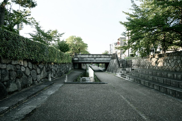 堀川沿いは遊歩道として整備されていて、堀川通からところどころで橋の下へ降りられるようになっている。写真は御池通の一筋北の押小路通あたりで、目の前に見えているのが二条通に架かる橋。/ 2025.06.28 堀川から