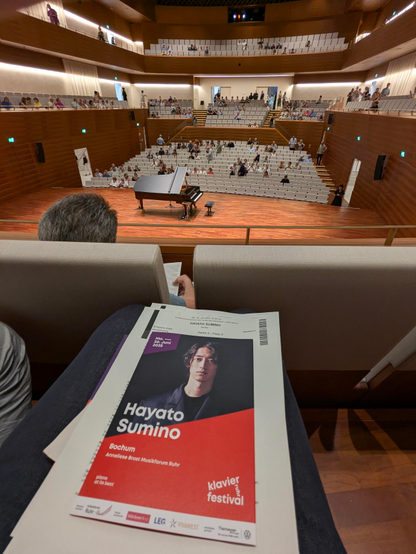 Der große Saal des Anneliese Brost Musikforums in Bochum von der Empore gesehen.
Im Vordergrund habe ich das Programm des Abends auf dem Schoß liegen. 
In der Mitte die Bühne mit einem Steinway Flügel.
Dahinter die anderen Zuschauerreihen.
Es war 20min vor Beginn.
Die Reihen sind also noch nicht gefüllt. 