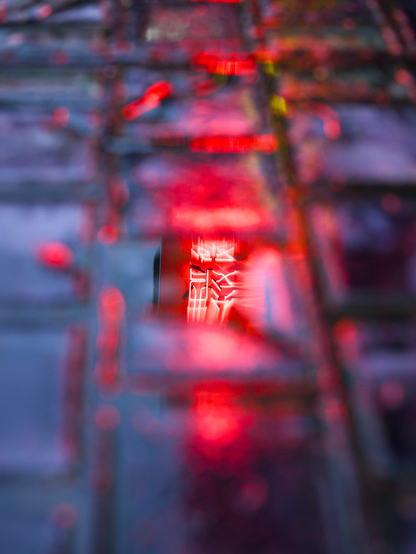 Rainwater pooling on paving blocks creates a small puddle in which the red neon lights and oriental writing from a restaurant are reflected
