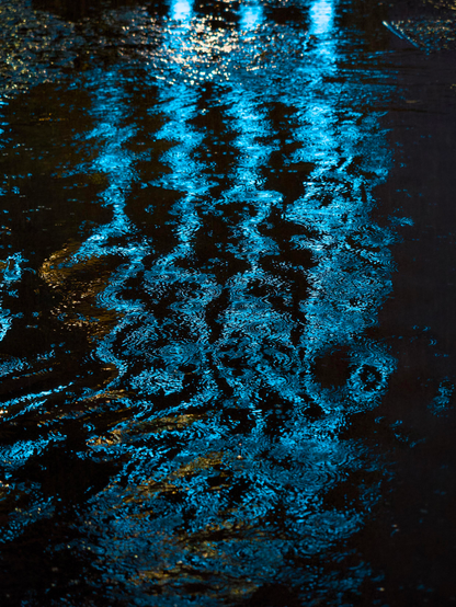 Blue neon lights from a tower block hotel on Argyle Street are reflected in a large puddle and as traffic drives past the reflection is warped, creating distorted ripples