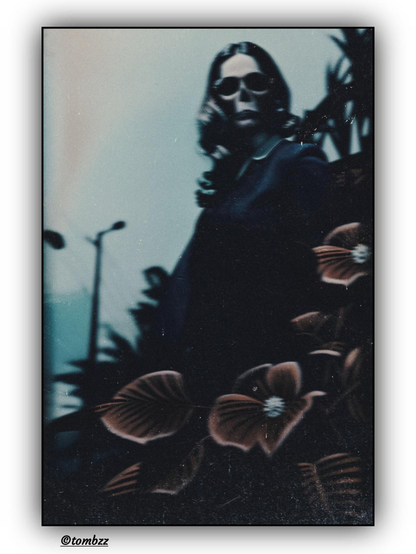 A figure resembling a woman, dressed in dark clothing with a white collar, photographed from below against a bright sky. Her face is hidden behind a mask and sunglasses, giving her an eerie and alien appearance. In the background, there is a streetlamp and the shadow of a building, while in the foreground, a large-leaved plant adds depth to the composition. The image shows signs of editing, stylized to resemble an old photograph inspired by horror cinema.