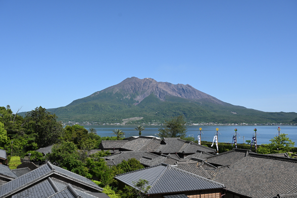 青い空に桜島がそびえている.
その手前には、錦江湾そして仙巌園の瓦屋根が写っている.