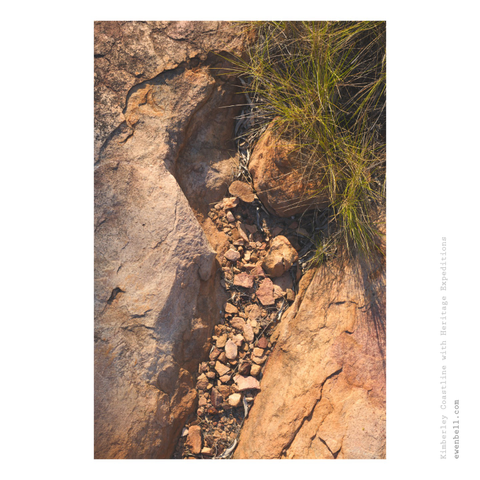 A carve out of sandstone, where smaller rocks gather and the spinifex begins to overgrow.