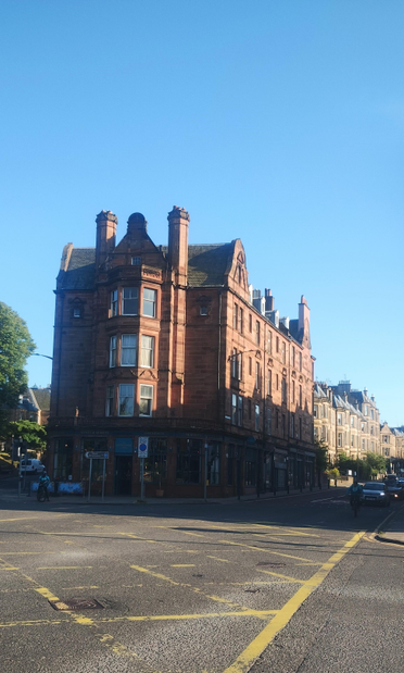 Four storey, Victorian, red stone tenement with bar on front ground floor, standing at a junction with two roads forking down either side of it