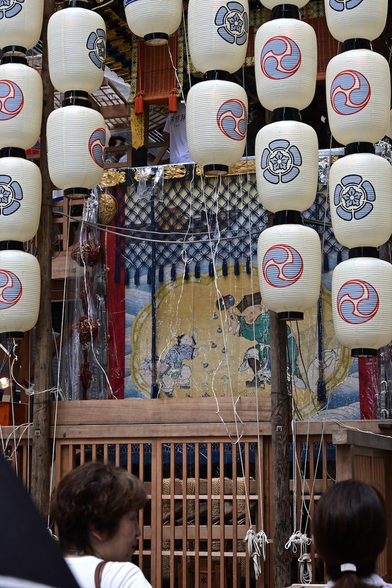 菊水鉾の前掛け。胴掛け・見送りと合わせて七福神が描かれているうちのゑびす神と大黒天。ちなみにゑびす神は屋根の上にいるので、前掛けにはゑびす神の烏帽子が置かれている様子が描かれている。すだれに隠れて見にくいけど。/ 2025.07.16 菊水鉾町から