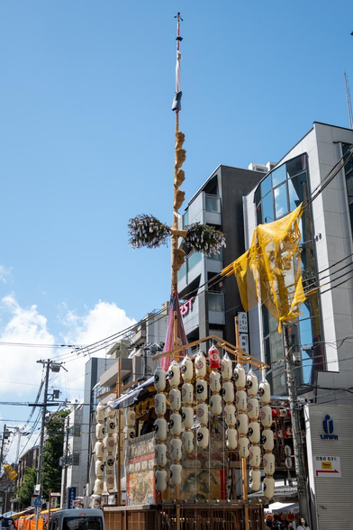 京都経済センターの西隣に位置する鶏鉾。鉾頭は三角形の中に円が描かれた模様で、堯の時代に天下が治まり諫鼓が利用されなくなって鶏が住み着いた故事をモチーフとしている。/ 2025.07.15 鶏鉾町から