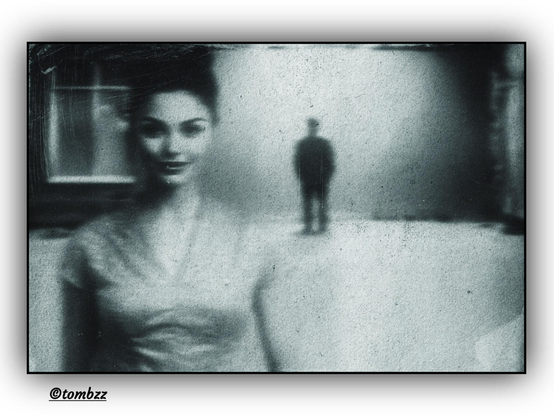 Black-and-white photograph taken with analog film, featuring a deliberately blurred frame that evokes cinematic aesthetics. In the foreground, a dark-haired woman — her face and figure softly outlined, with her hair partially cropped by the edge of the image. In the background, to the right, stands a man — his silhouette dark, mysterious, almost shadow-like. On the left side, a double-winged window subtly illuminated, adding depth to the space. The entire composition carries a retro or vintage mood, reminiscent of the French New Wave — embracing imperfection, formal freedom, and poetic everydayness. The image radiates nostalgia, ambiguity, and visual intimacy.