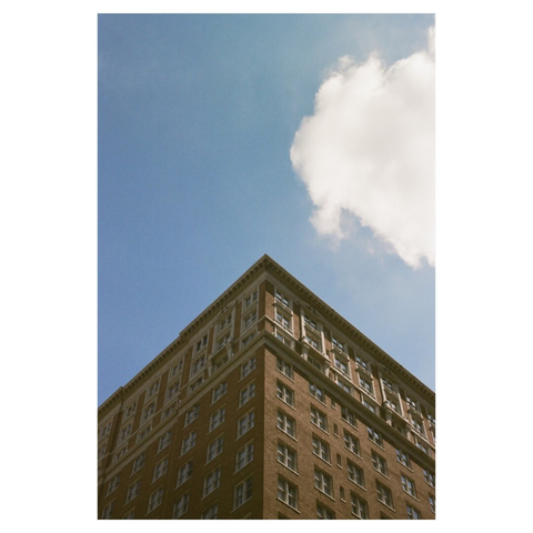 the corner of a building looking up with a cloud set against a blue sky.
