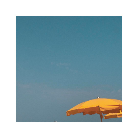 a tiny yellow sun umbrella is sitting in the bottom right corner of the square image. all the rest of the frame is just focusing on the crystal clear turquoise sky