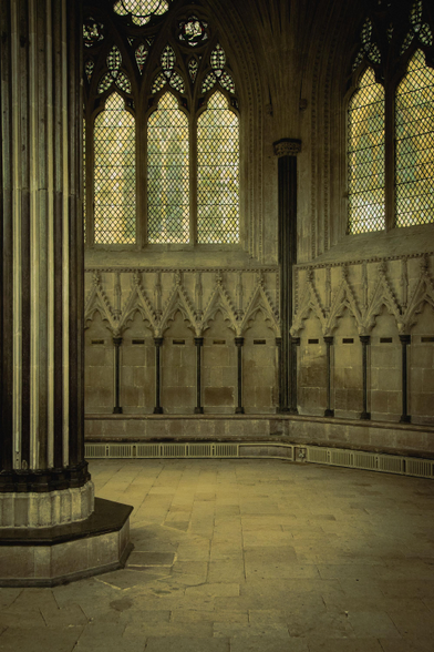 Inside the Chapter House: an ornate pillar, stalls carved out of stone, and arched windows.