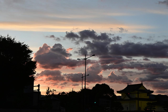 二条城前から日の入り直前の夕暮れ雲。空の低いところと雲の明るい部分が赤く染まっている。/ 2025.07.27 堀川通御池角から