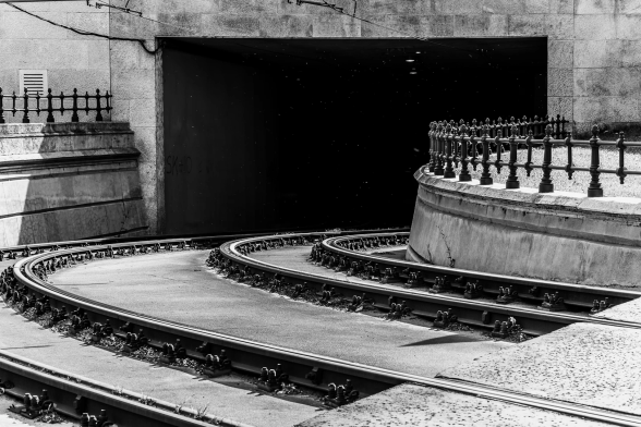 In eine rechteckige Straßenunterführung verlaufen in sanfter Kurve zwei paar Straßenbahnschienen. An den Seiten wird alles von Geländern im Kurvenverlauf flankiert. Viel Geometrie.