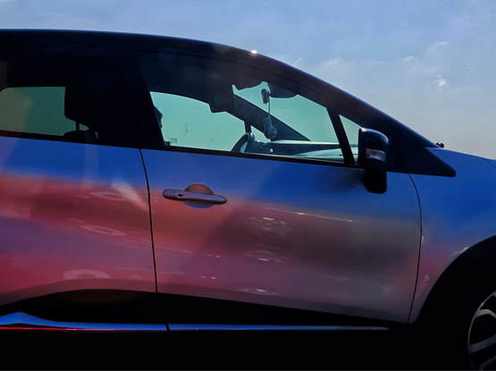 The side profile of a car with a gradient paint job transitioning from blue at the top to purple/pink at the bottom. The effect comes from the reflection of a red car in the side of the blueish one.