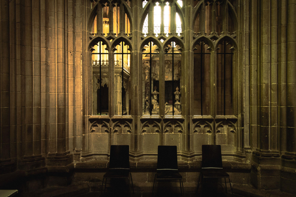 Interior of a gothic cathdedral: three modern chairs in front of three arches.