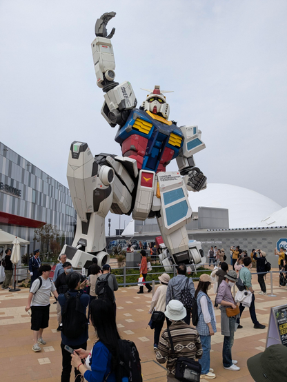 Der Gundam Roboter hat eine Hand in d3n Himmel gehoben und ein Knie auf dem Boden.